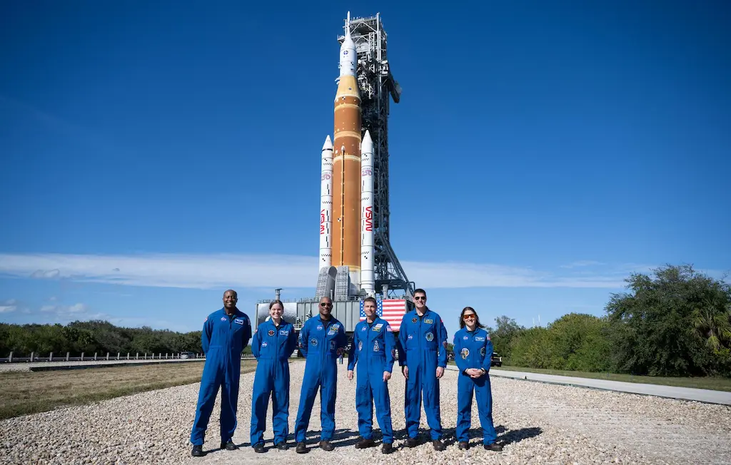 Tripulação principal e reserva da missão Artemis II posam em frente ao foguete SLS e cápsula Orion na plataforma de lançamento móvel no Centro Espacial Kennedy da NASA.