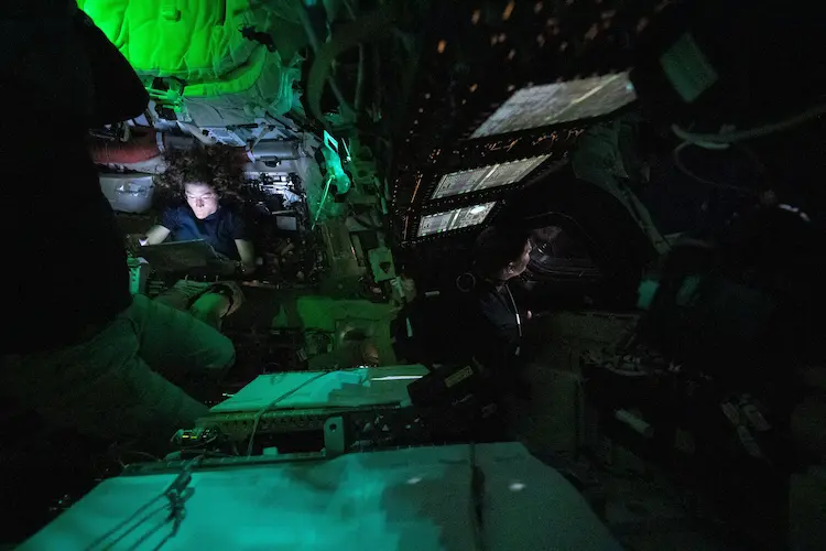 A astronauta da NASA, Christina Koch, &eacute; iluminada por uma tela dentro da espa&ccedil;onave Orion, que est&aacute; escura, no terceiro dia da miss&atilde;o Artemis II da ag&ecirc;ncia. &Agrave; direita do centro da imagem, o astronauta da CSA (Ag&ecirc;ncia Espacial Canadense), Jeremy Hansen, &eacute; visto de perfil olhando por uma das janelas da Orion. As luzes est&atilde;o apagadas para evitar reflexos nas janelas.