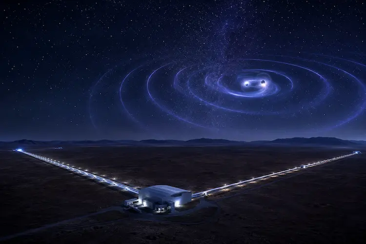 Observat&oacute;rio de ondas gravitacionais em paisagem des&eacute;rtica &agrave; noite, com bra&ccedil;os iluminados de interfer&ocirc;metro e ondula&ccedil;&otilde;es c&oacute;smicas no c&eacute;u representando a fus&atilde;o de objetos compactos.