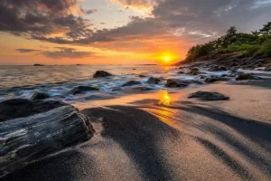Praia de Guarapari com faixas de areia escura rica em minerais pesados, rochas costeiras e mar ao pôr do sol.